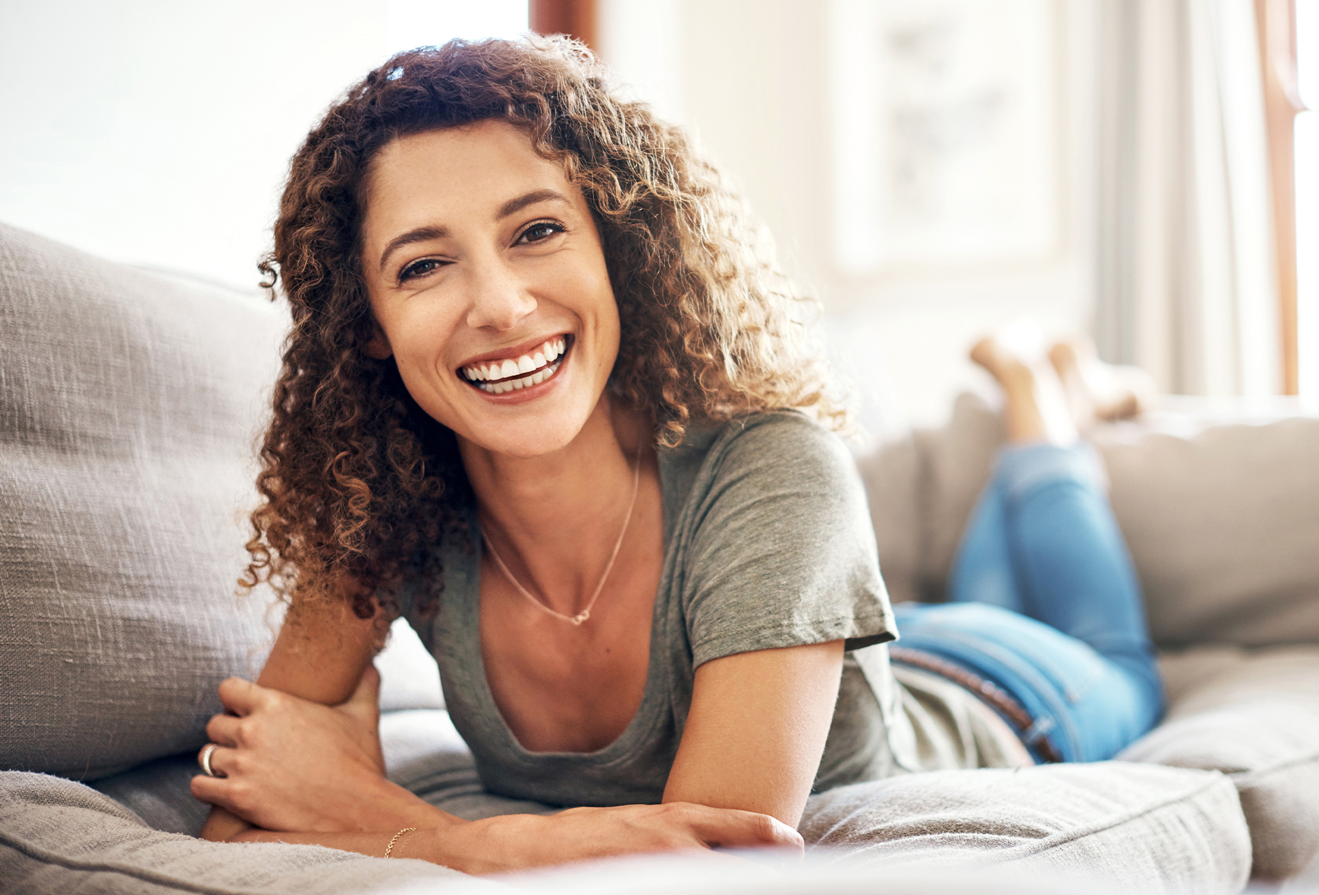 woman with curly hair smiling while laying on a couch