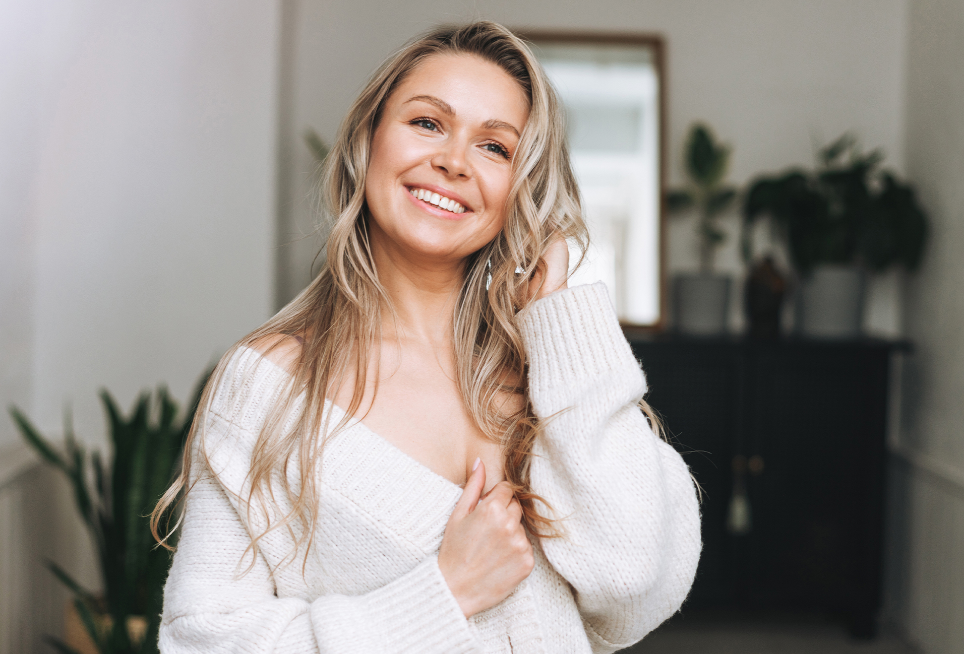 Woman with blonde hair smiling, wearing an oversized white sweater