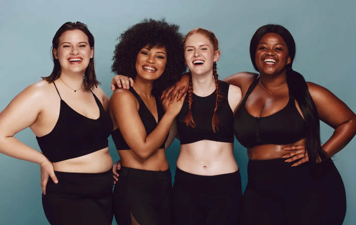 Group of four women with differing body types and skin tones wearing athletic clothing and smiling