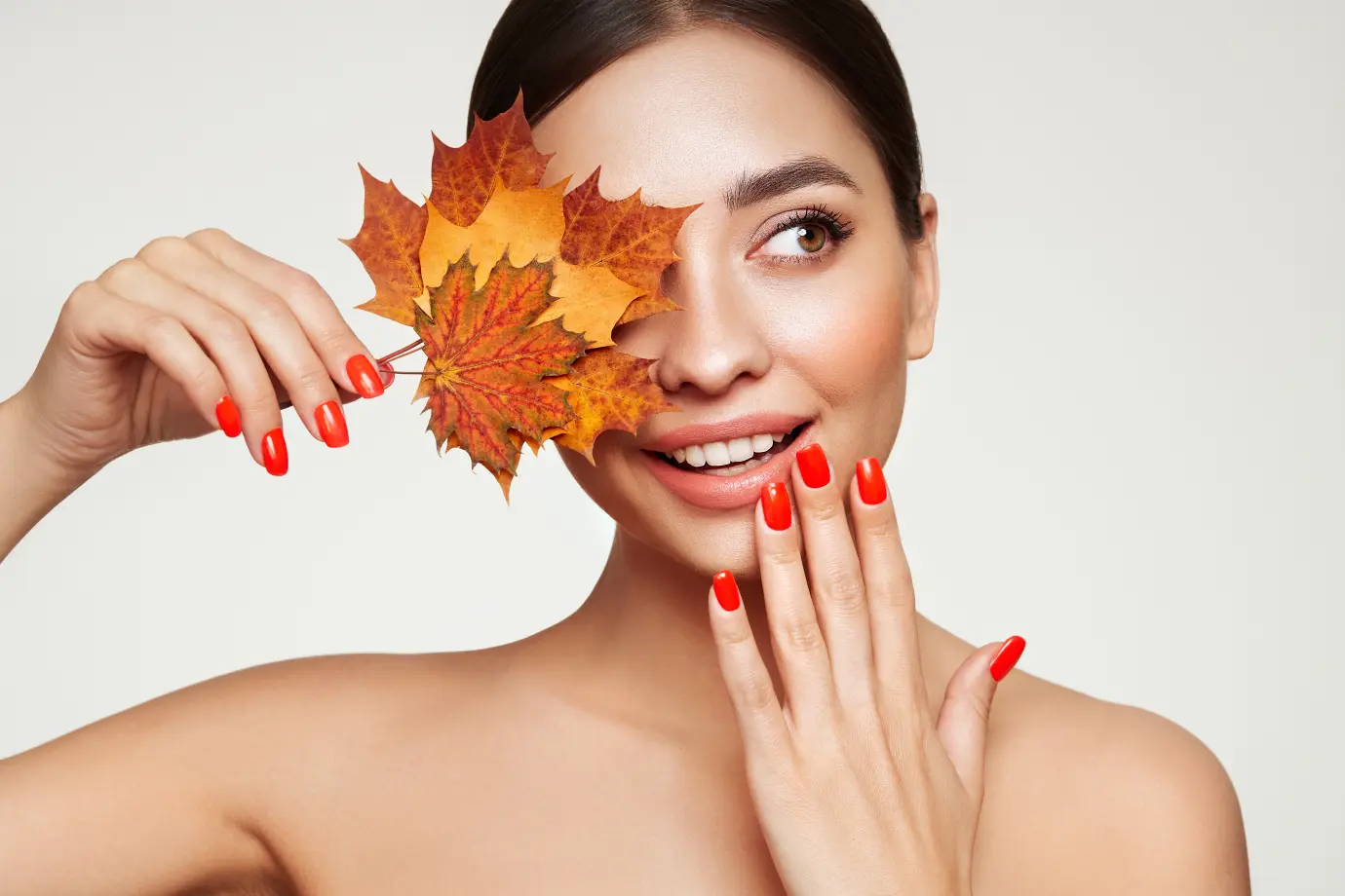 A woman with an orange and yellow leaf held up against left eye, smiling.