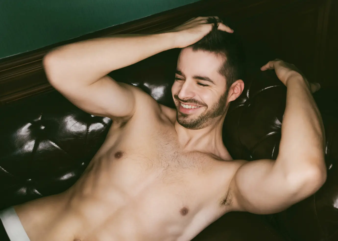 Man laying on sofa shirtless smiling running hand through hair