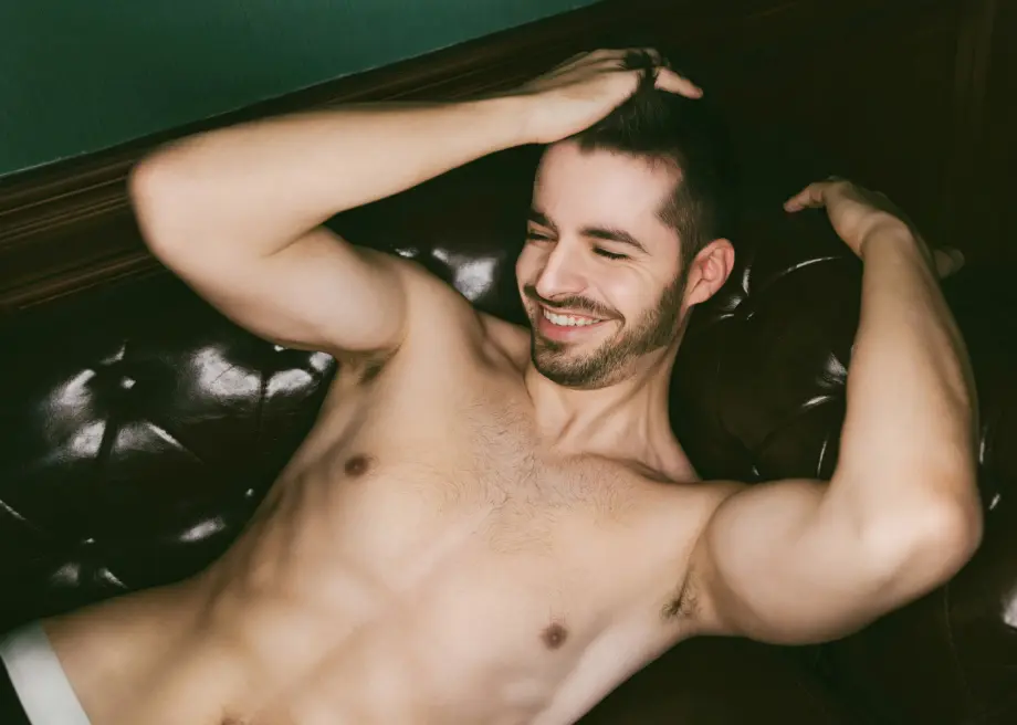 Man laying on sofa shirtless smiling running hand through hair