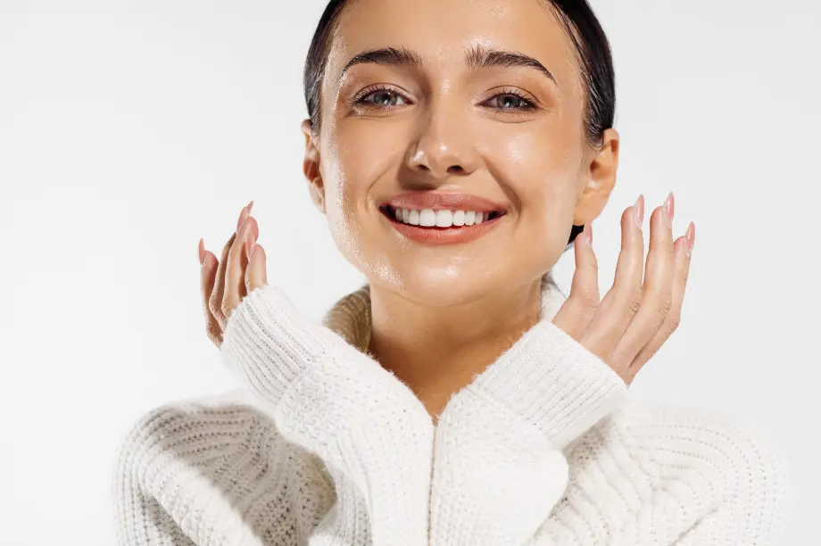 A woman wearing a white sweater, smiling, with glowing skin