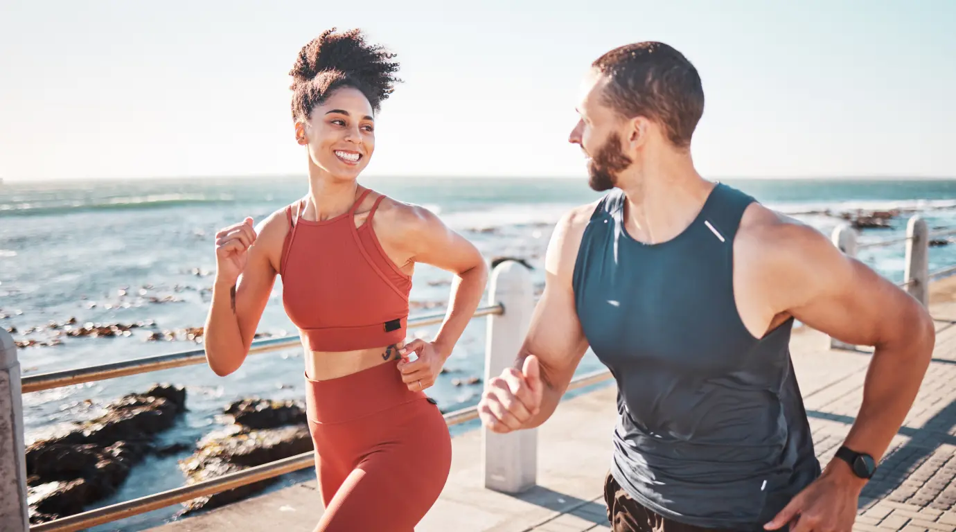 Man and woman wearing athletic clothing running along coast on boardwalk