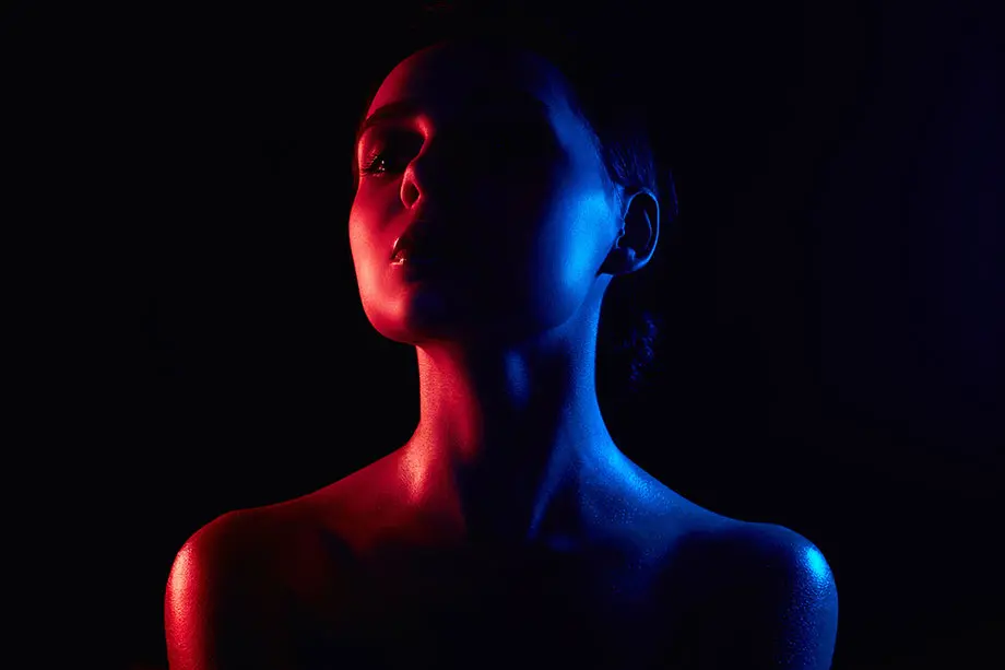 Woman in dark room illuminated by subtle red and blue light